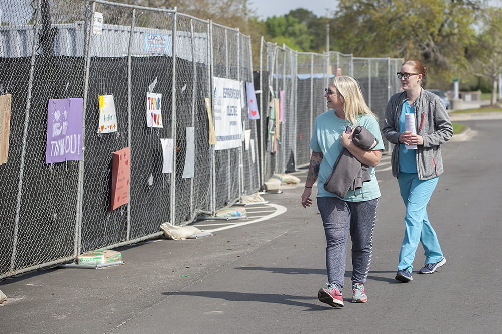 MUSC Health employees look at encouraging messages on fence at drive-through specimen collection site at Citadel Mall.