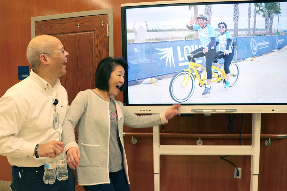 A man and woman laugh at a picture on television screen.