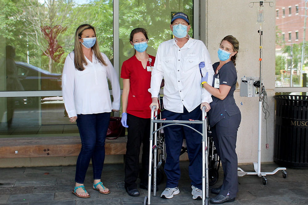 Nurse Emerald Turner and occupational therapist Kelly Rishe help John McDonald stand as Lisa McDonald watches his progress. 