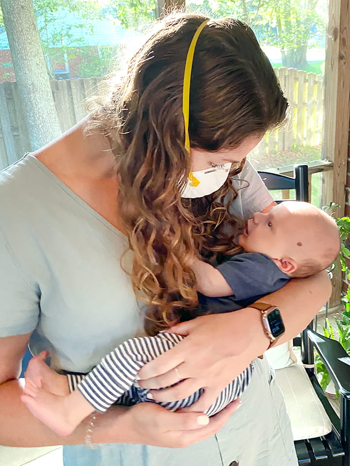 A woman wearing an N95 mask holds a baby