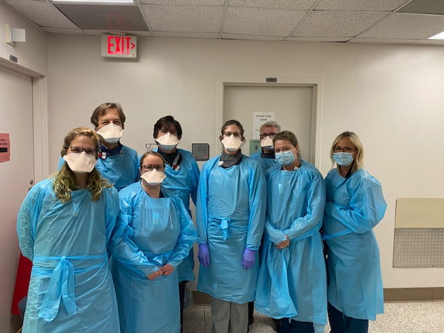 A group of masked and gowned health providers pose in a hallway 