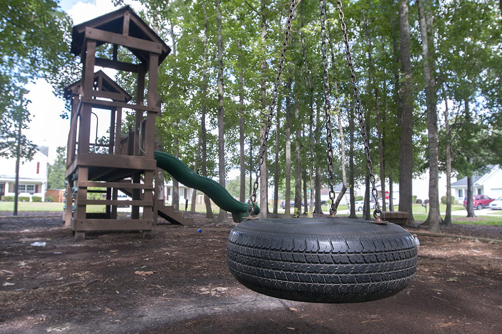 an empty tire swing hangs in front of a deserted play structure