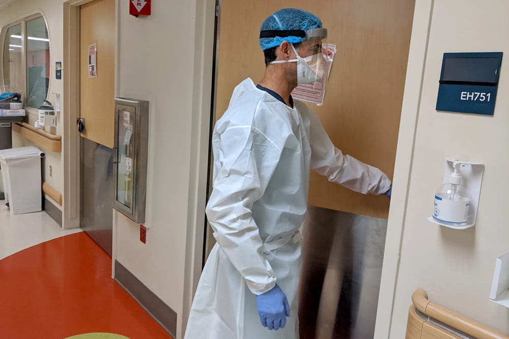 a nurse in gloves, gown, hairnet, mask and face shield enters a patient room