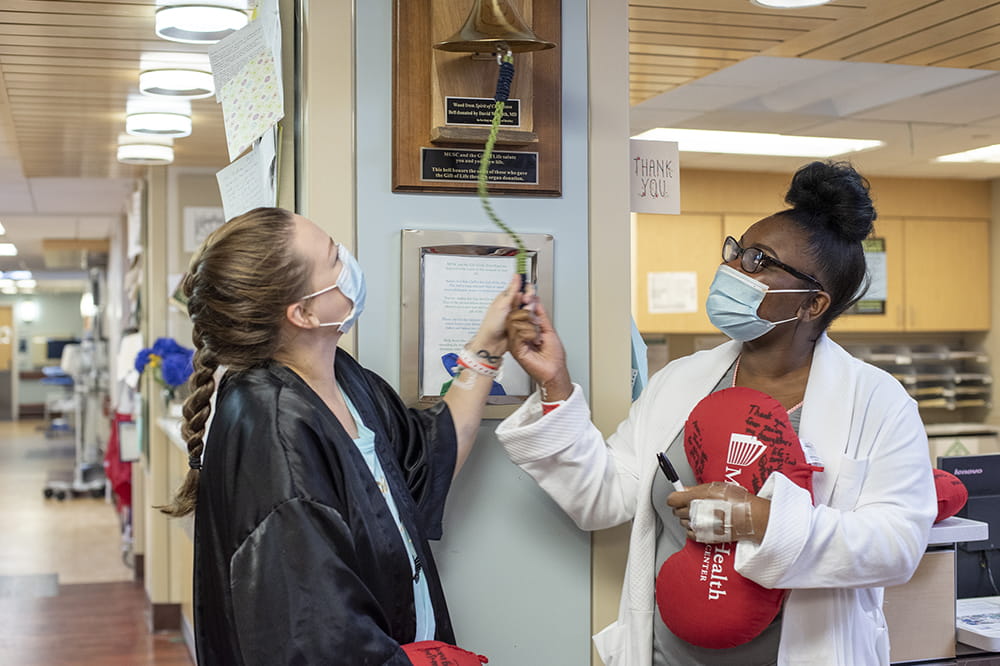 two young women together pull the cord on a bell attached to the wall to ring it