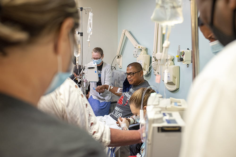 people in a hospital treatment room hold hands in a circle and pray