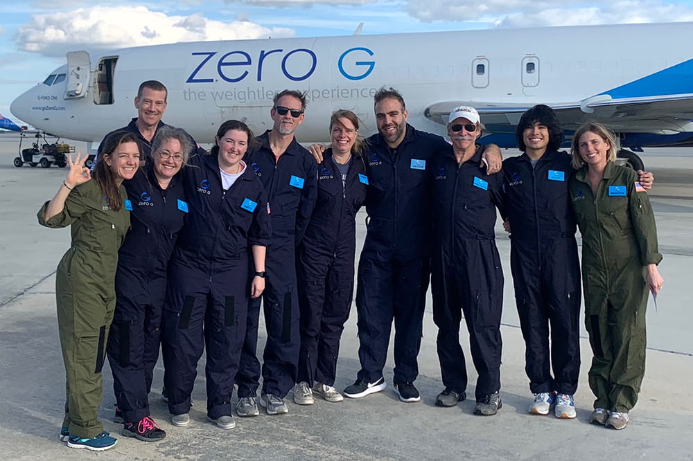 the team stands in flight suits in front of the Zero G plane on the tarmac