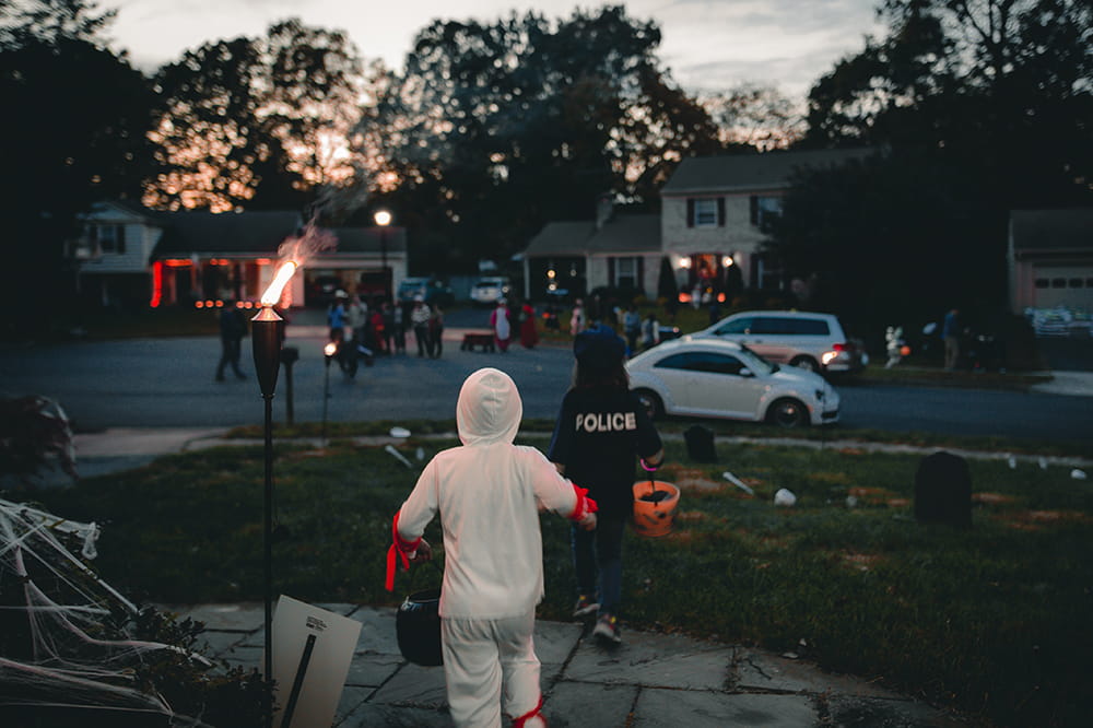 A twilight image of children in costumes running around a suburban neighborhood trick or treating