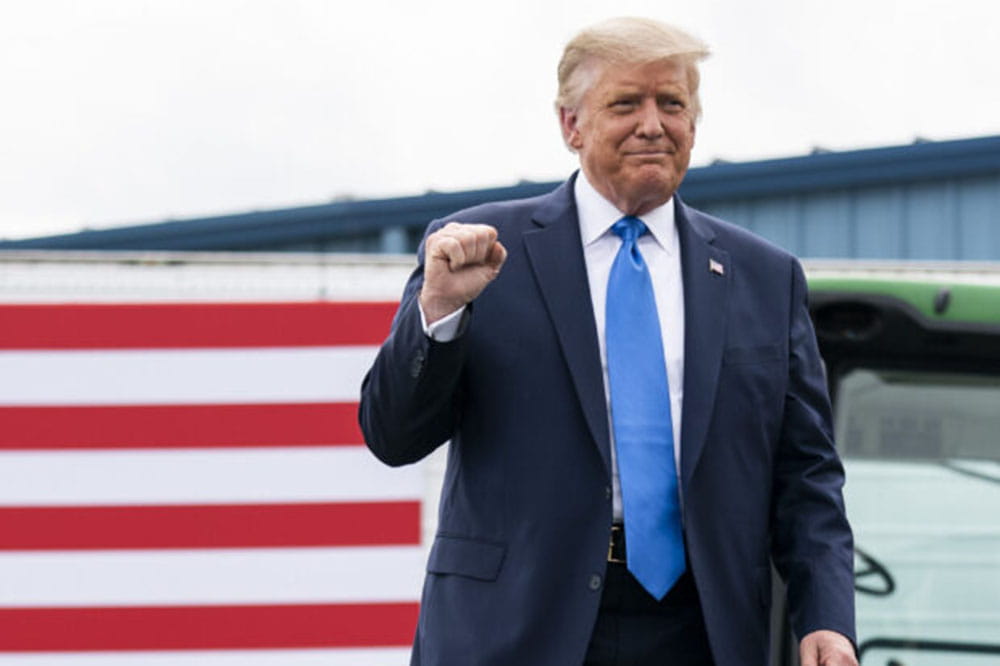 President Trump stands in front of a flag raising his fist.