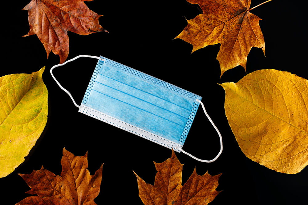 Surgical mask on a black background surrounded by autumn leaves