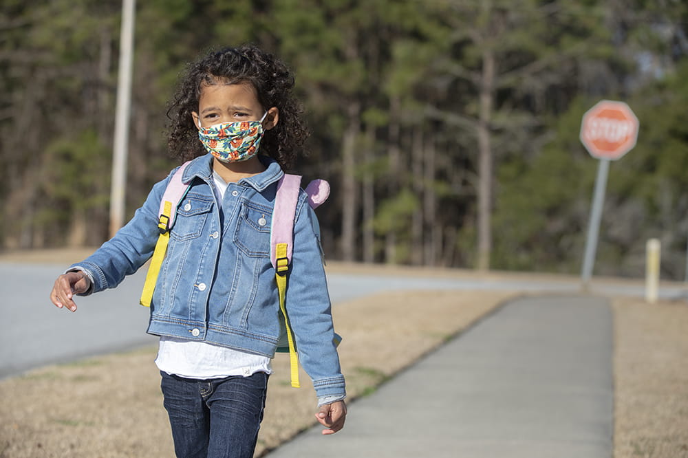 Girl walking to school wearing backpack and mask during coronavirus pandemic.