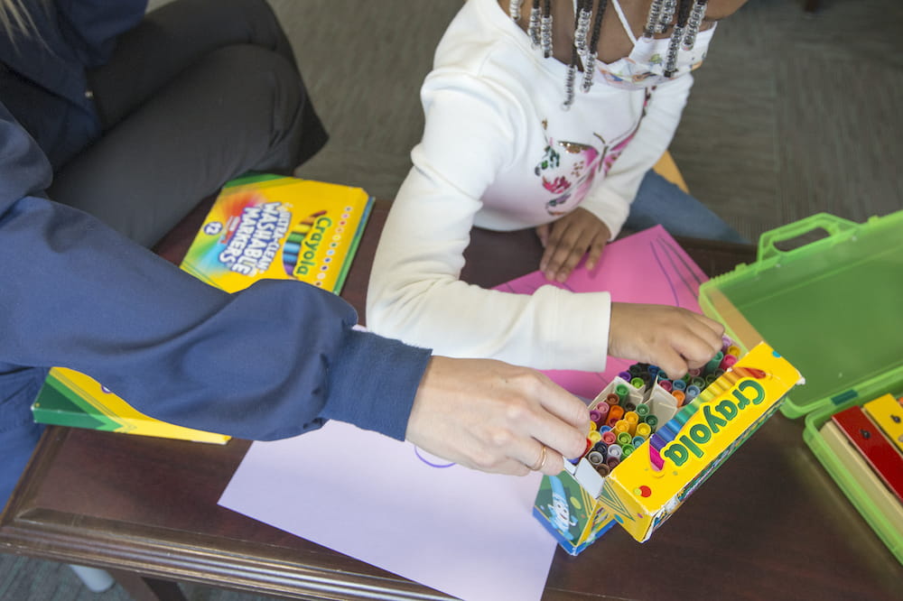 A health care worker and a child use markers to draw pictures