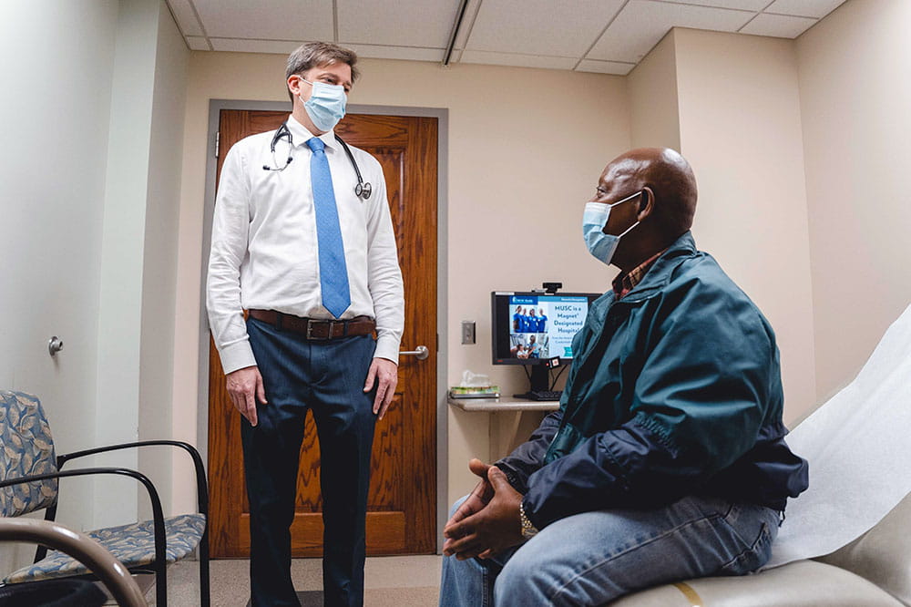Dr. Todd Gourdin talks with a patient in an exam room while both wear masks