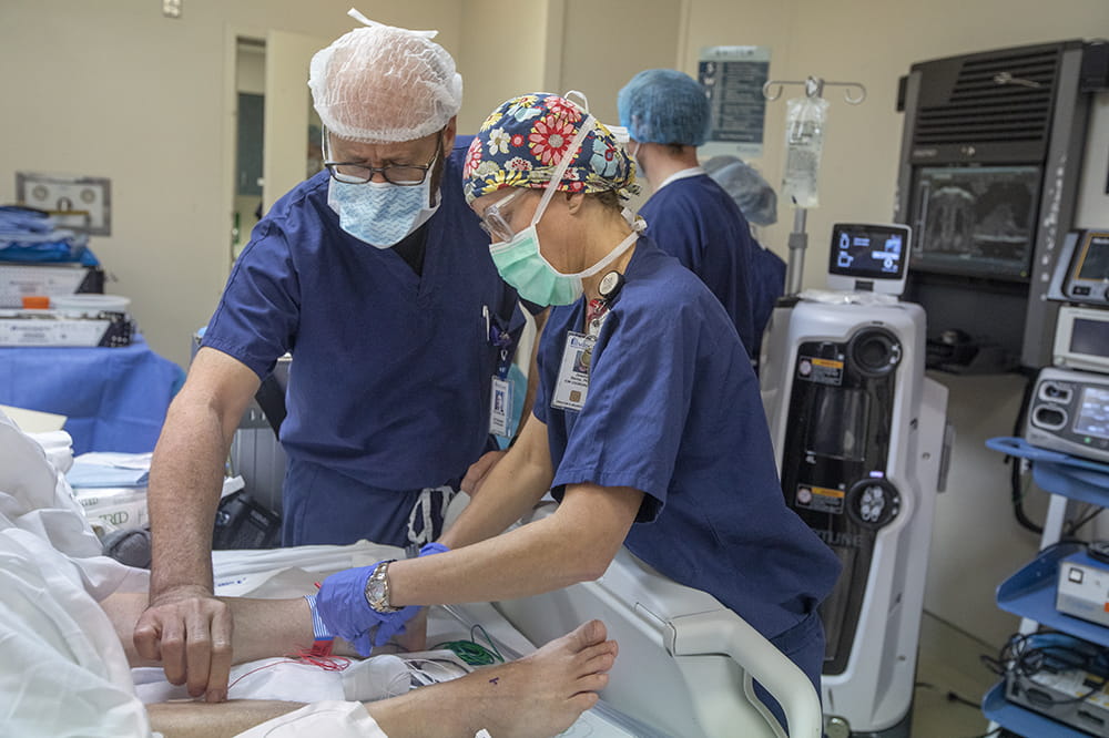 two people in operating room garb stand over a patient's legs