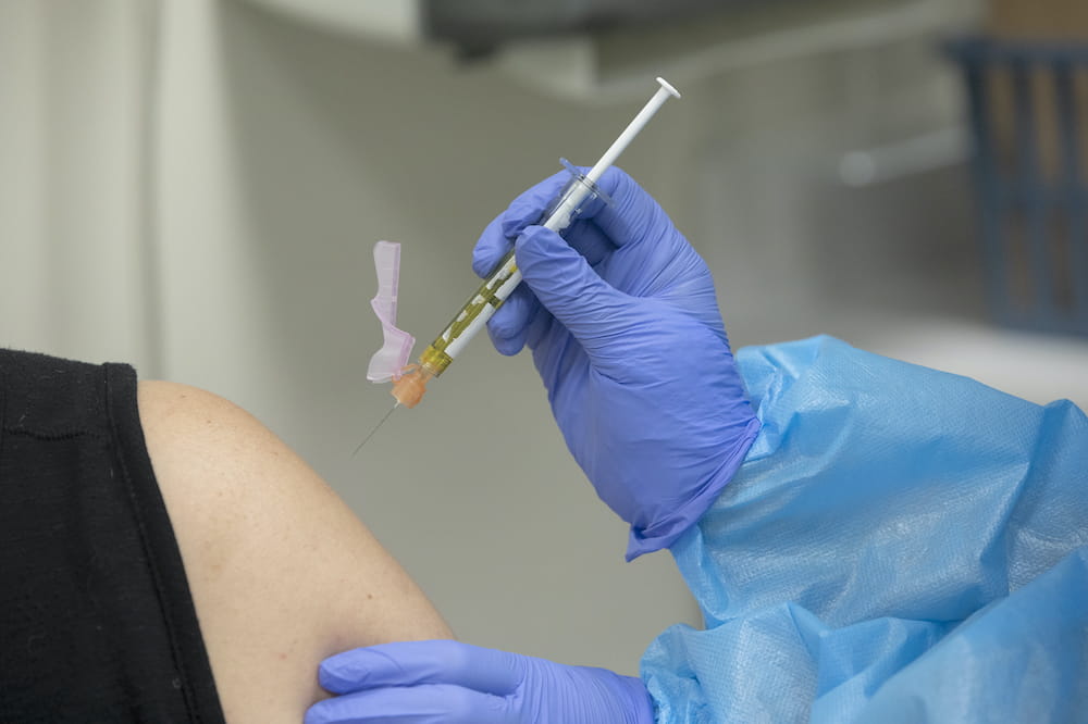 Syringe filled with vaccine about to be injected into upper arm
