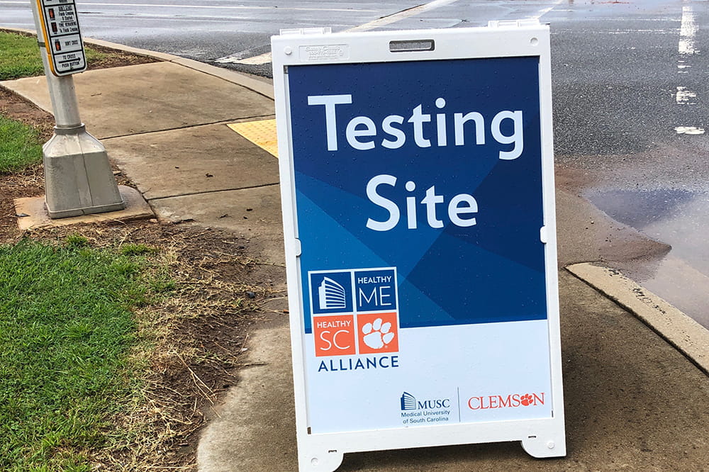 Sandwich board sign on a sidewalk says "testing site" and has the Healthy Me Healthy SC logo 