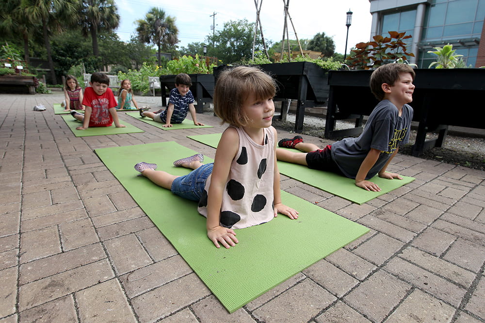little kids practice cobra pose on yoga mats in an outdoor garden space