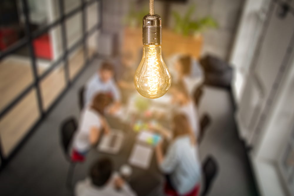 A lightbulb superimposed upon a conference room with people meeting to discuss ideas. Licensed from istock.com