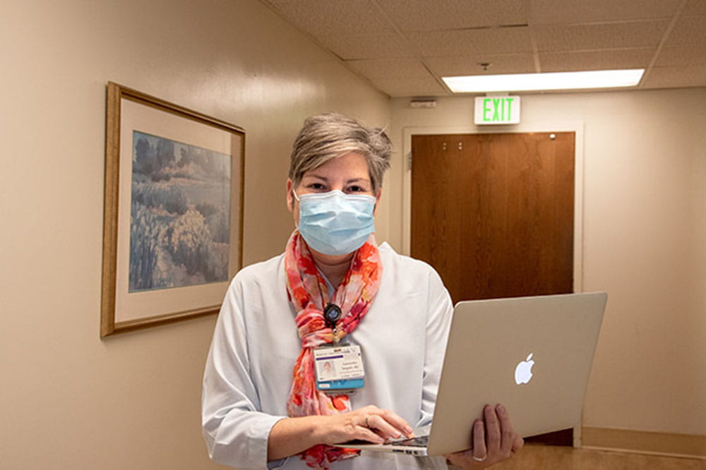 Dr. Cassy Salgado holds a laptop while wearing a mask during COVID-19 pandemic.