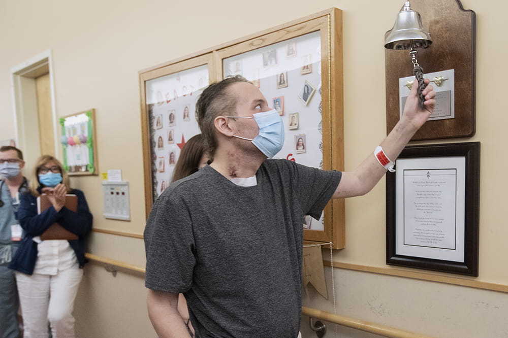 a man in a hospital hallway rings a bell mounted on a plaque