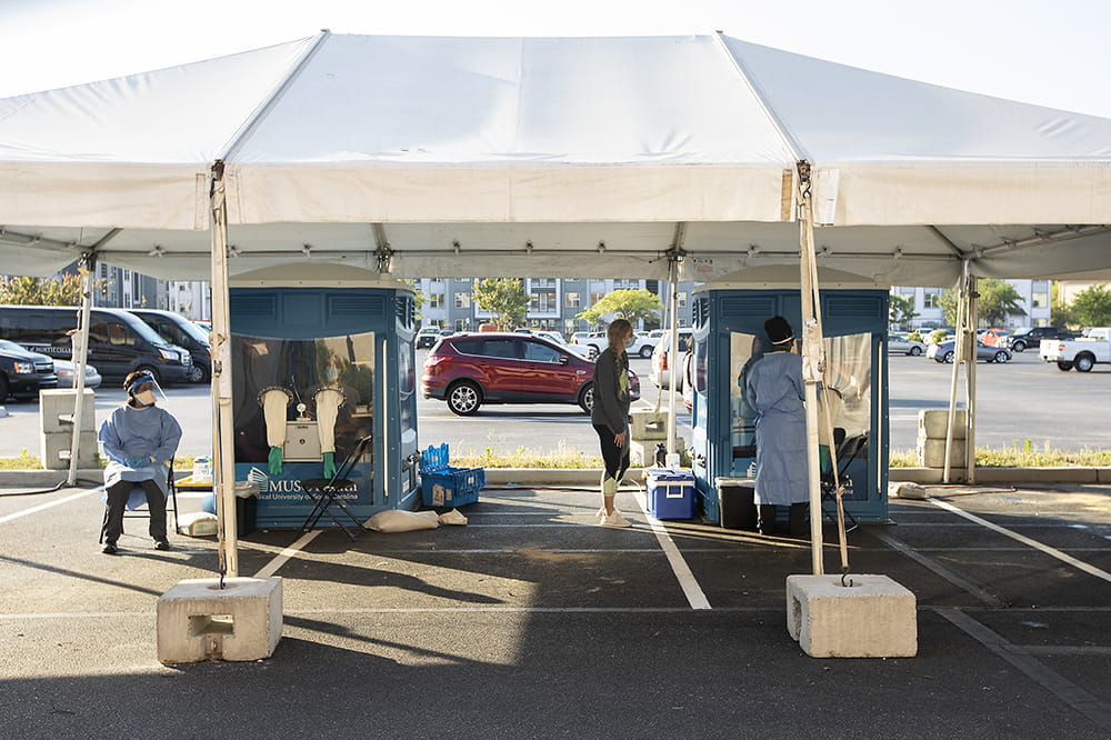 health car workers await next to portable testing pods under a tent