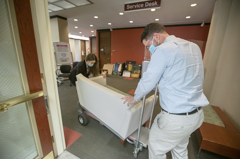 two people use a cart to wheel a loveseat out of a nearly empty library space
