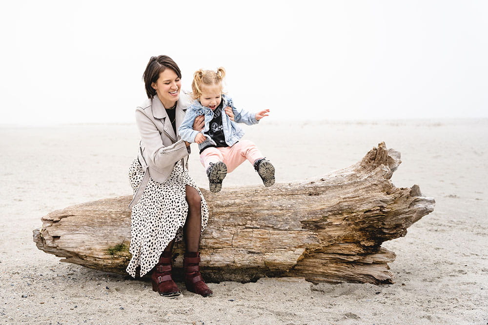 Liza Patterson helps her daughter jump off log on the beach