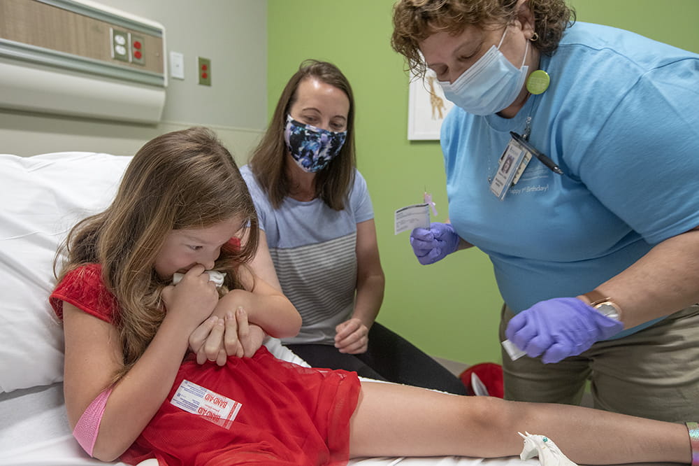 Nurse Karen Hawkins prepares to gives Alice Zwolak her first dose of the Moderna vaccine while the girl's mother, Pam Juranas Zwolak, holds Alice's hand.