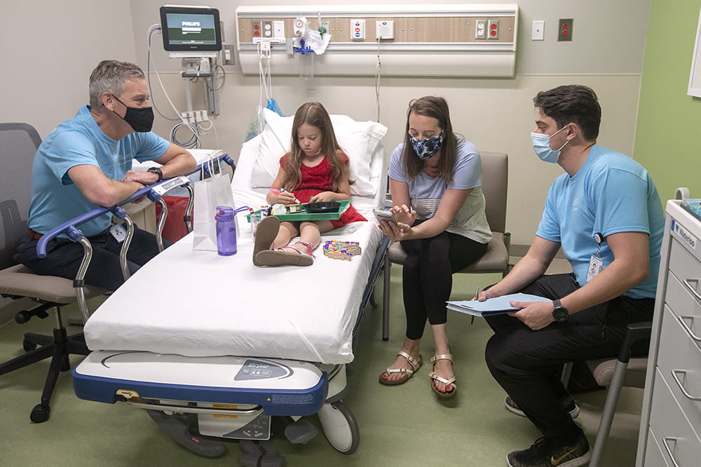 Alice Zwolak does a craft supplied by the Child Life specialist as Dr. Andrew Atz and program coordinator Kreighton Milks talk with her mother about what to keep an eye out for after Alice's first shot.