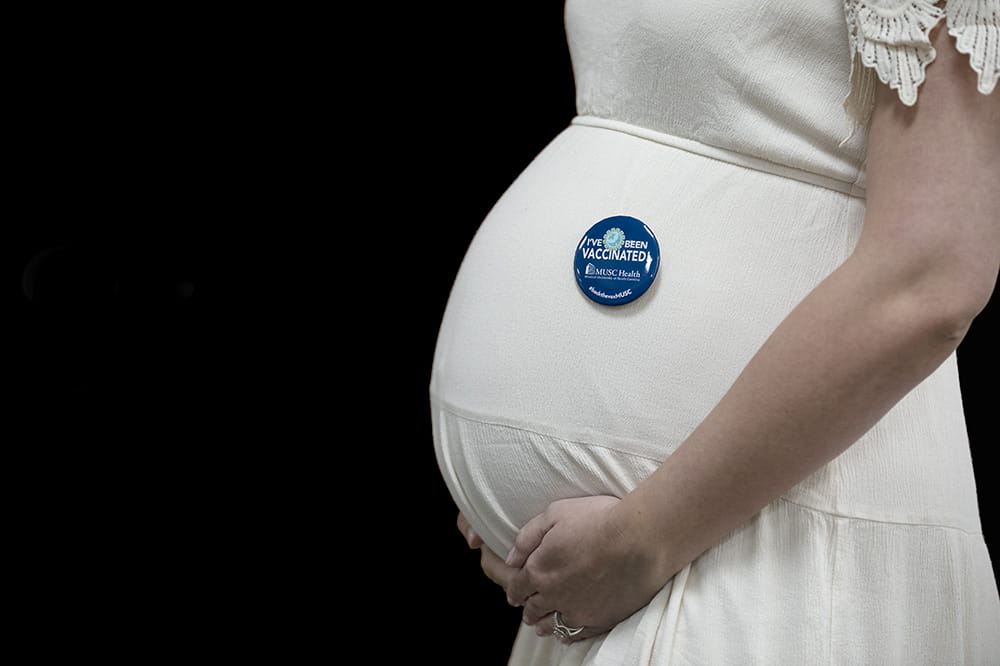 close up of a woman's pregnant belly. pinned on her dress is a button saying she is vaccinated