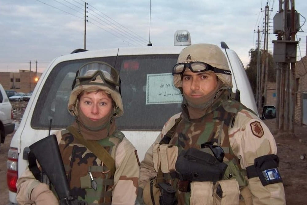 Two armed soldiers holding rifles and wearing helmets while standing behind an SUV
