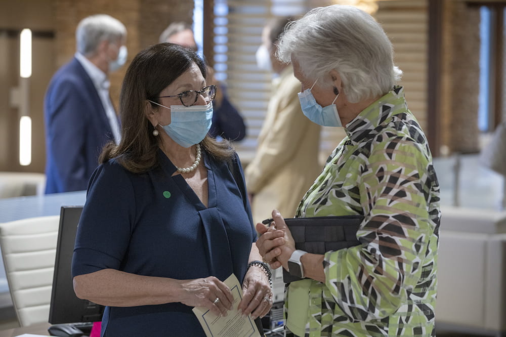 two nicely dressed women chat while wearing surgical masks