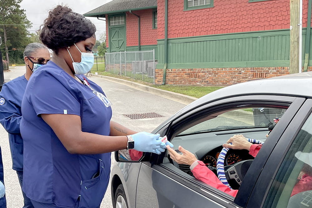 a woman in blue scrubs pricks the finger of a woman in the drivers seat of a car