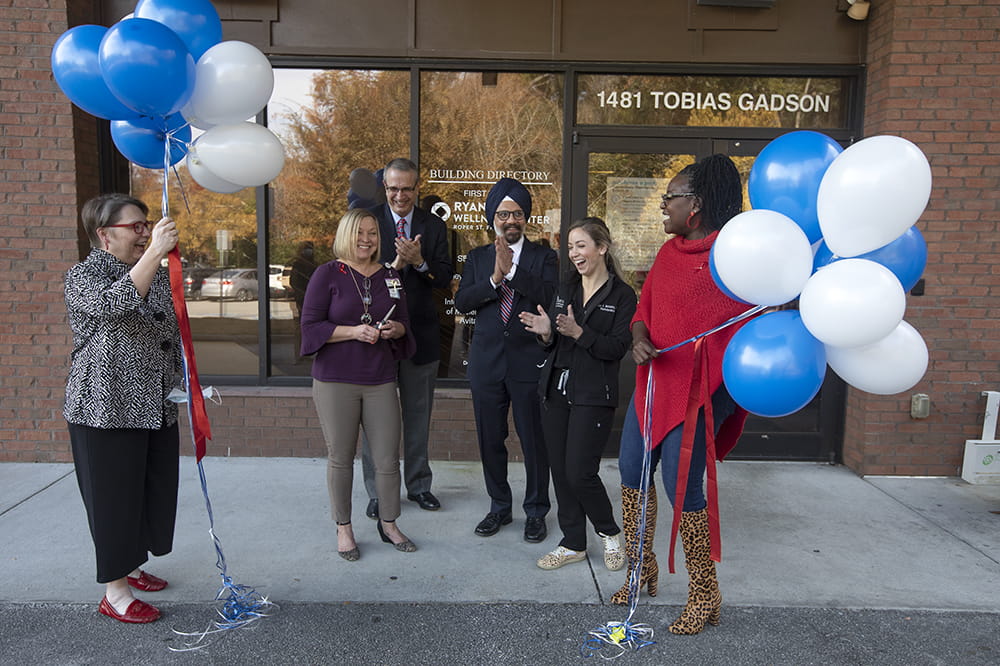 people laugh and clap after a ribbon is cut in front of the building