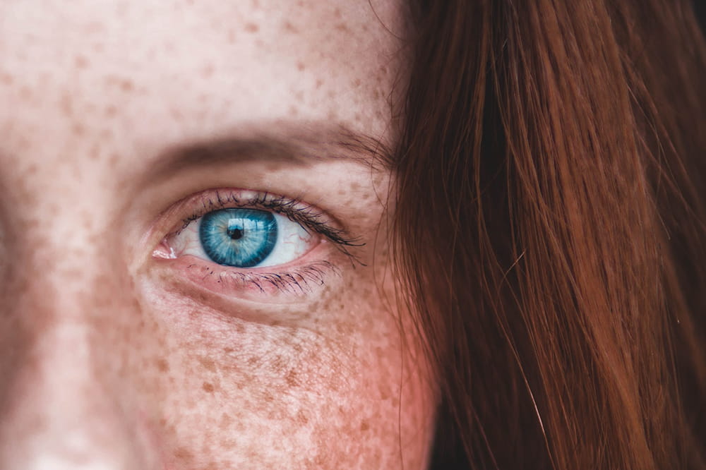closeup of a woman's piercing blue eye, freckled cheek and red hair