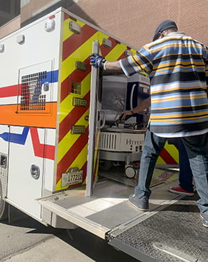 a facilities worker guides the mri into the back of the ambulance