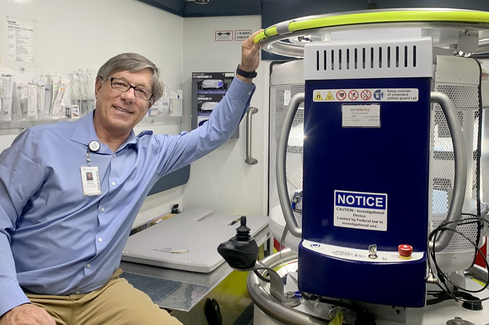 a man in khakis and blue button down shirt poses with the MRI inside the ambulance