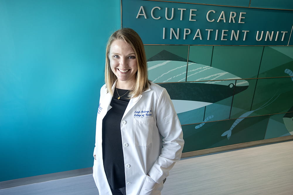 portrait of a woman in a white lab coat in front of acute care inpatient unit entrance