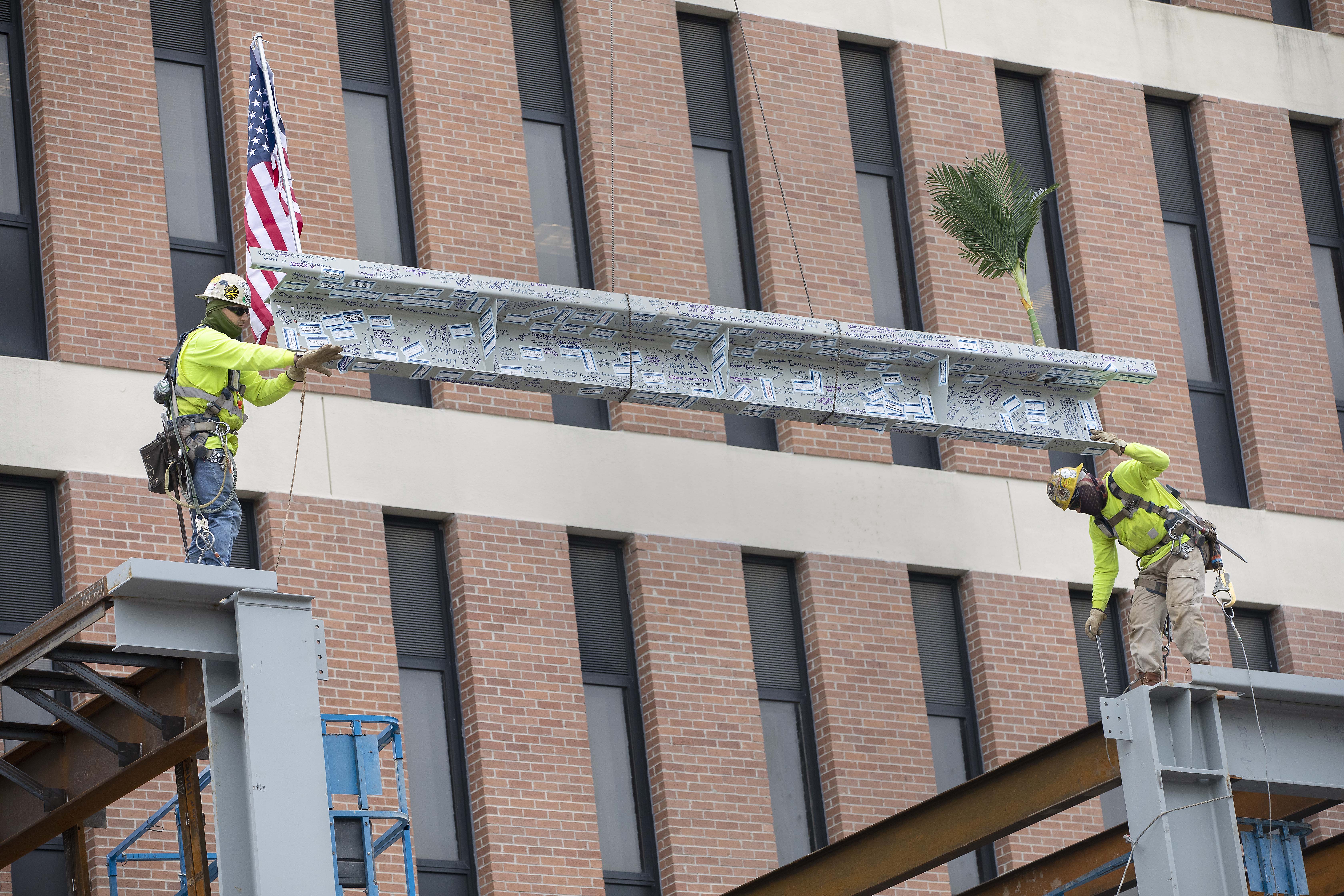 Construction workers place beam in topping out ceremony for the College of Pharmacy.