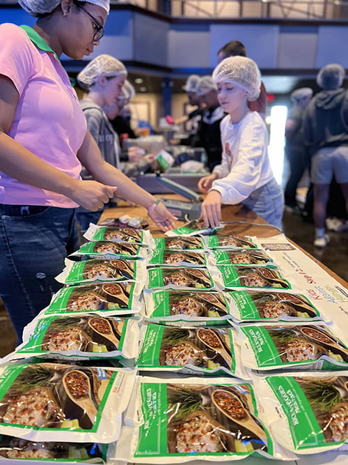 two young girls in hairnets work at a volunteer food packing table