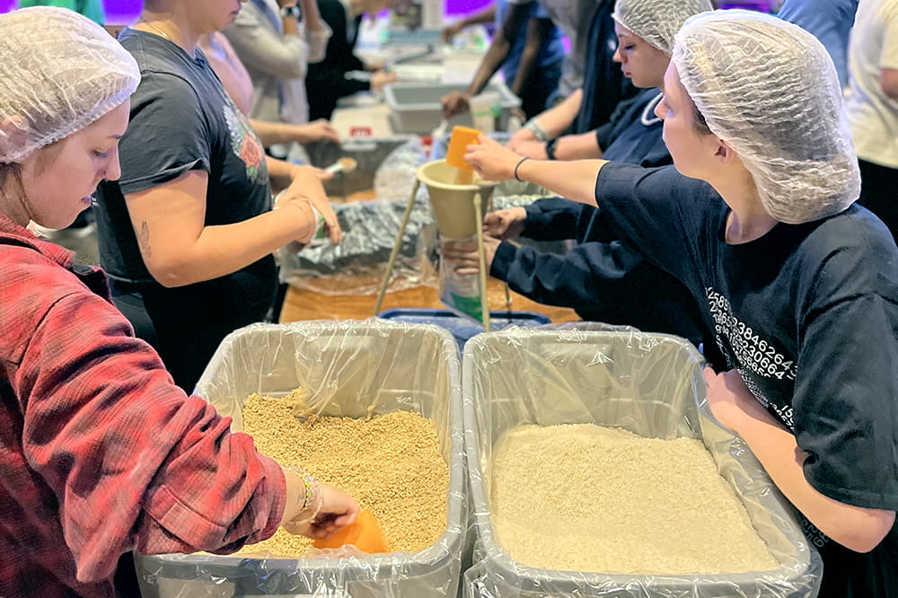 closeup of two women in hairnets on opposite sides of table scooping from large bins of rice