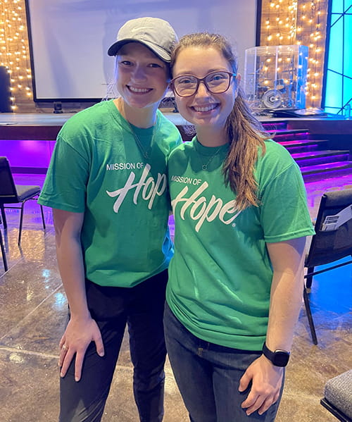 two women in green shirts that say Mission of Hope pose for the camera