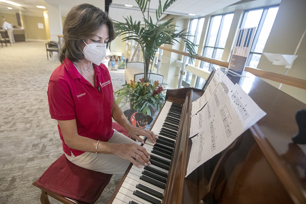 a woman in a red volunteer polo sits at a piano and plays