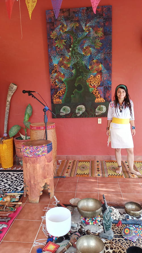 young woman standing in a colorful room of pink wall and terracotta floor with traditional drums and microphone set up as for a ceremony