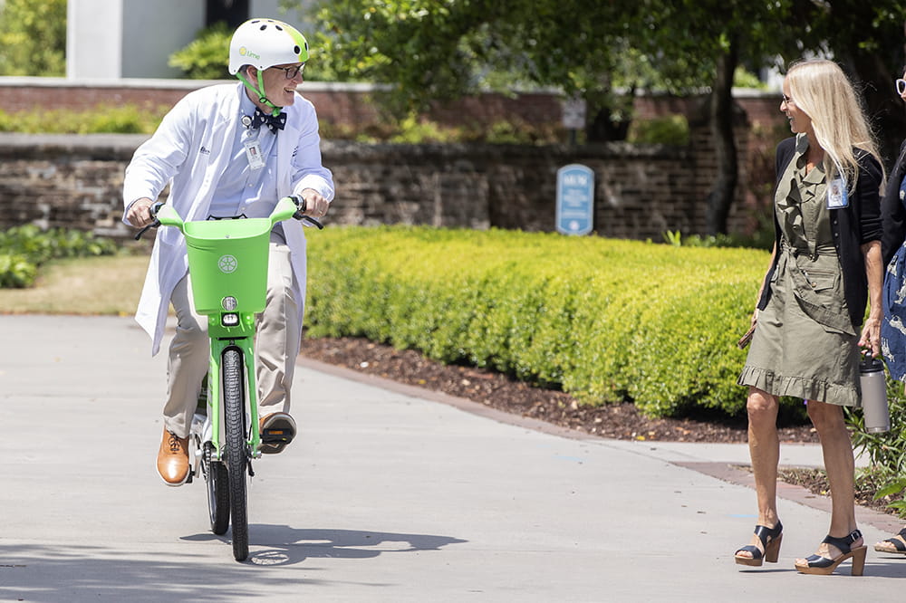 Doctor David Zaas rides an e-bike as Susan Johnson smiles nearby