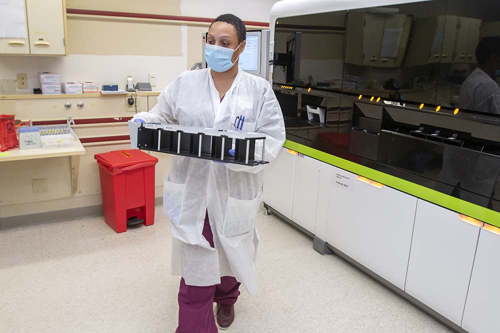 Clinical lab scientist Tanisha Dickerson carries a tray of materials involved with testing. 