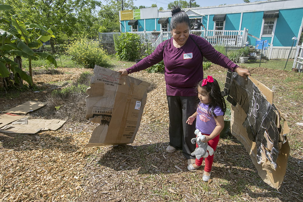 a woman stands with her arms to the side, holding two large pieces of cardboard, while her small daughter stands near her