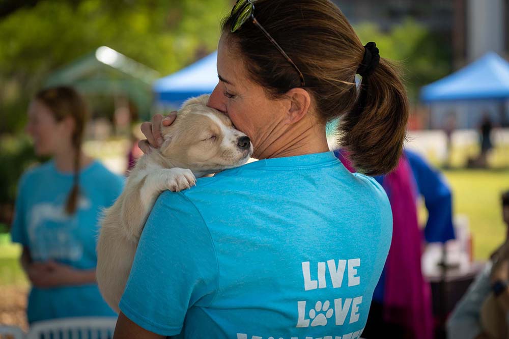 Woman in a blue t shirt holds a puppy.