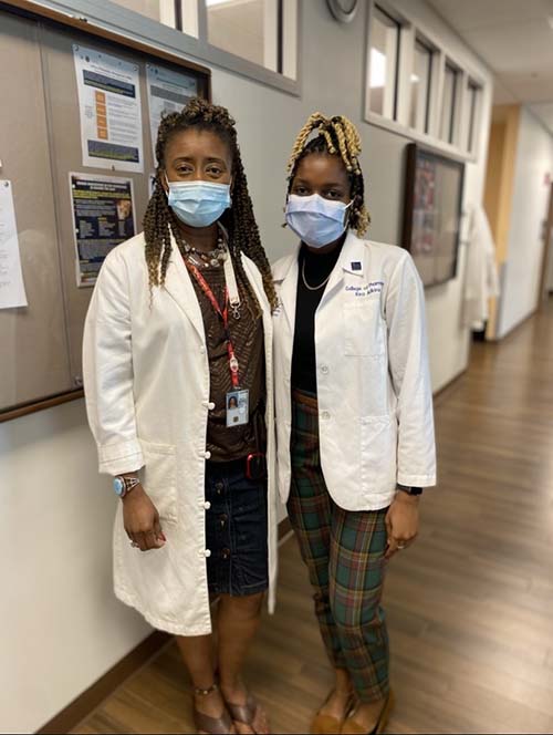 Dr. Erica Hanesworth with College of Pharmacy graduate Kira Adkins. Both are wearing masks to protect against COVID and white coats. 