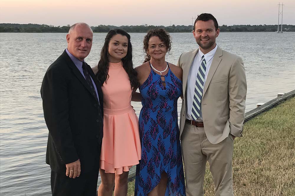 College of Dental Medicine student Keith Tormey with his sister and parents pose in front of water. He and his father are wearing suits. The women are wearing dresses.