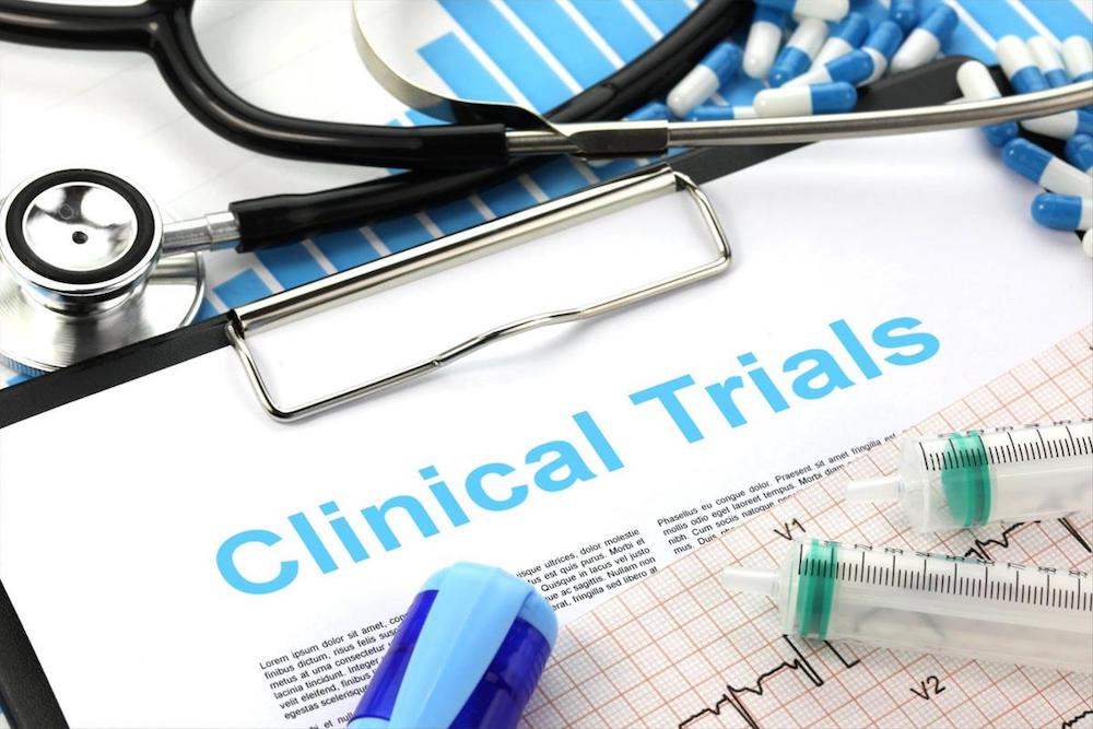 Binder saying clinical trials along with stethoscope, vials and pills.